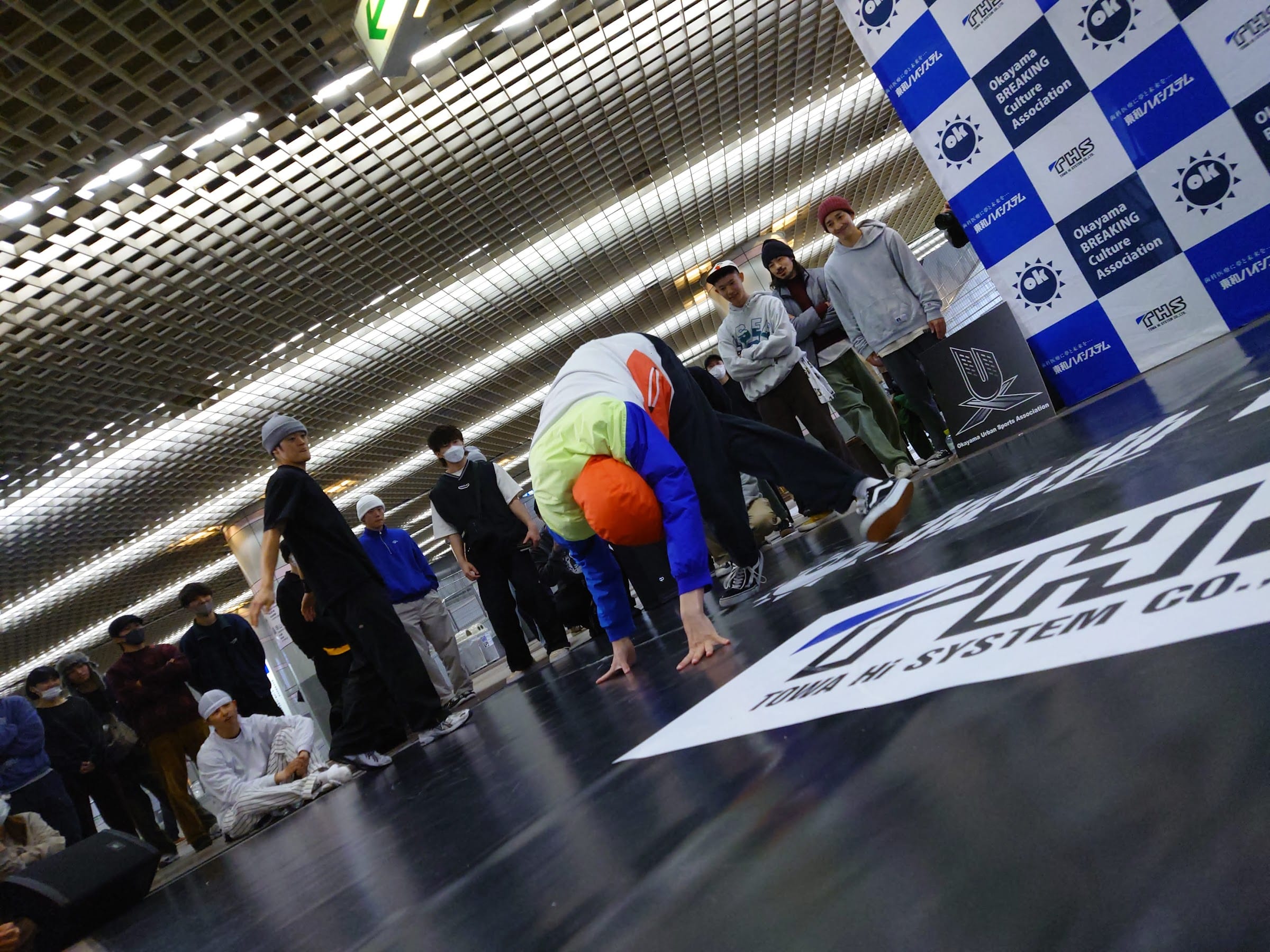 Dancer swiping across the TOWA HI SYSTEM sponsor floor graphic