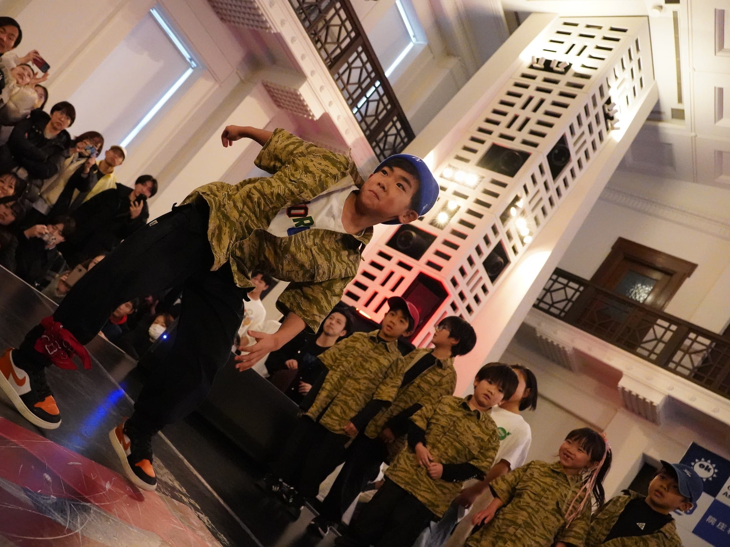 迷彩柄のお揃いユニフォームを着た控えメンバーの前で踊るダンサー